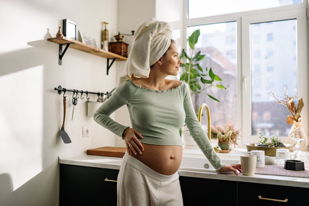 a-pregnant-woman-standing-with-hand-on-her-belly-7155635 Young pregnant woman enjoys morning in kitchen, gazing outside.