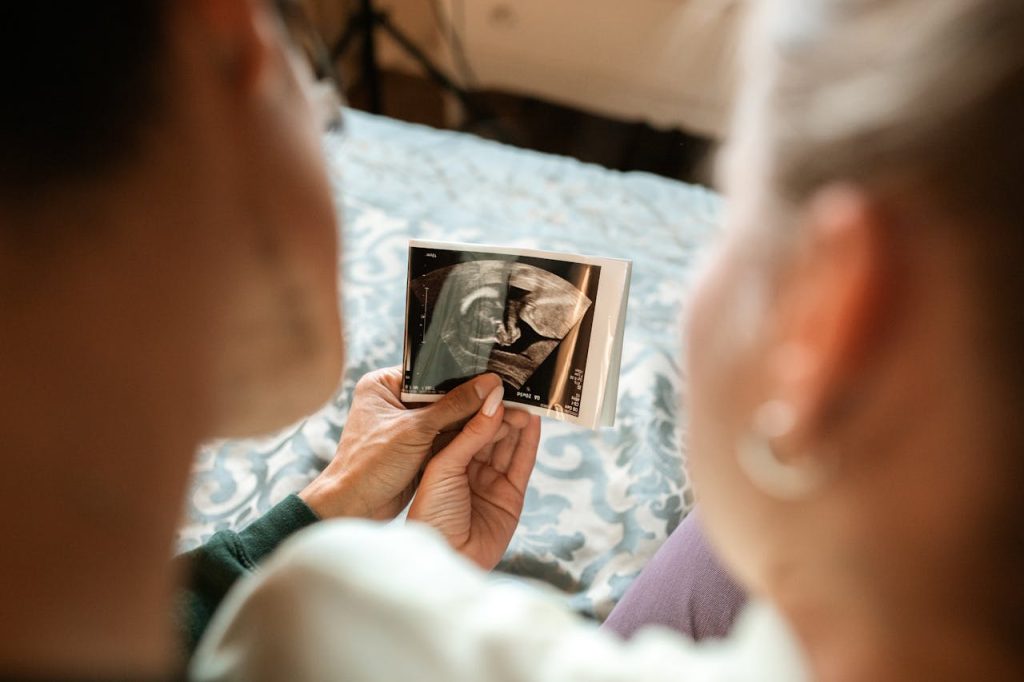 woman-in-white-long-sleeve-shirt-holding-photo-of-man-in-black-suit-6149306 Expectant parents sharing a tender moment viewing their babys ultrasound image.